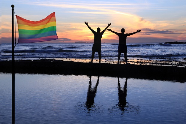 two people by ocean with rainbow flag