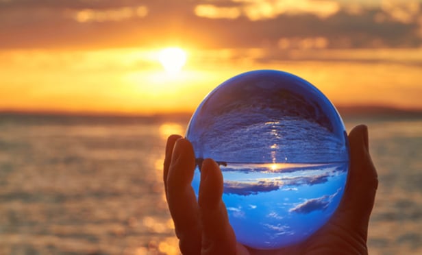 Hand holding crystal ball up against horizon at sunset