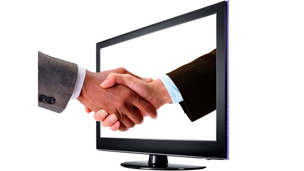Men shaking hands through a computer monitor