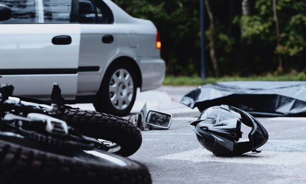 A photo showing the aftermath of an accident between a car and a motorcycle. The car sits in the background while a laid-out motorcycle and helmet lay on the pavement in the foreground. 