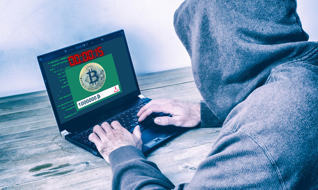 A hacker is shown from the back, wearing a hoodie, committing Bitcoin fraud on a laptop