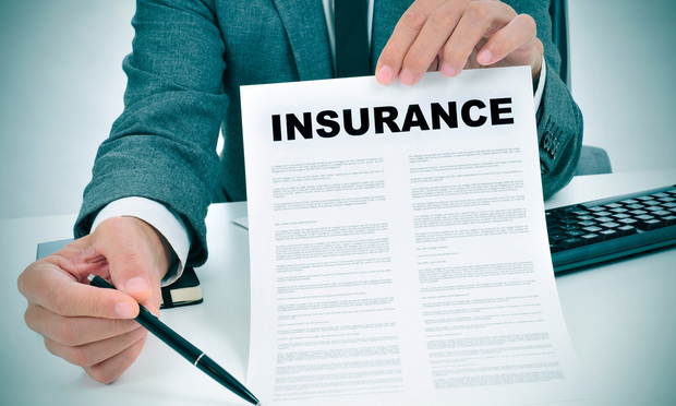 A person in a business suit holds a piece of paper that says "Insurance" in front of him in one hand, and an ink pen in the other.
