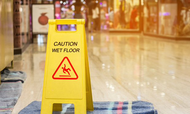 A wet floor sign sits on top of a towel on the floor of a mall.