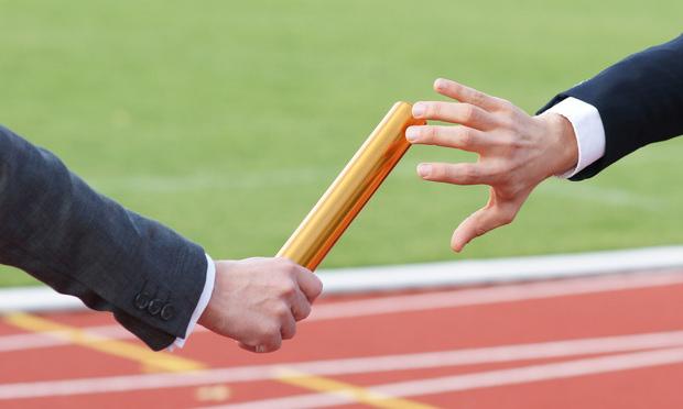 A businessman passes a baton to another as they run on a track.