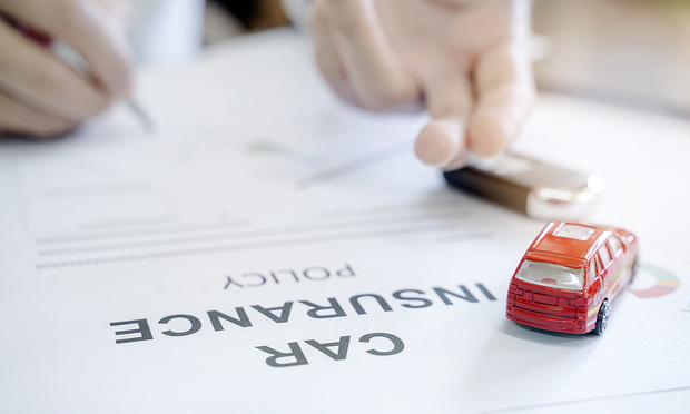 A red toy car sits on top of a car insurance policy as someone signs it.