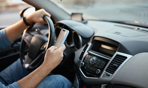 A person holds a phone in their hand, texting while they drive.