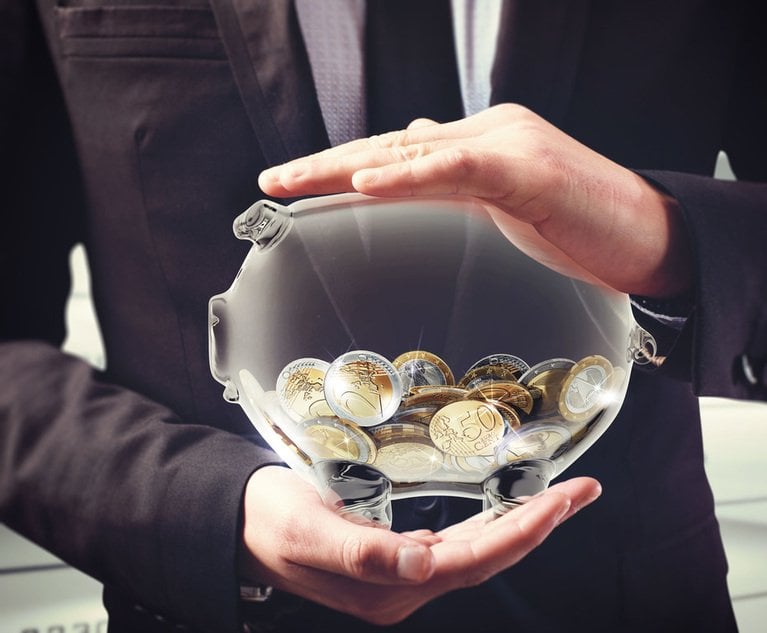 A businessman holds a clear piggy bank full of coins.
