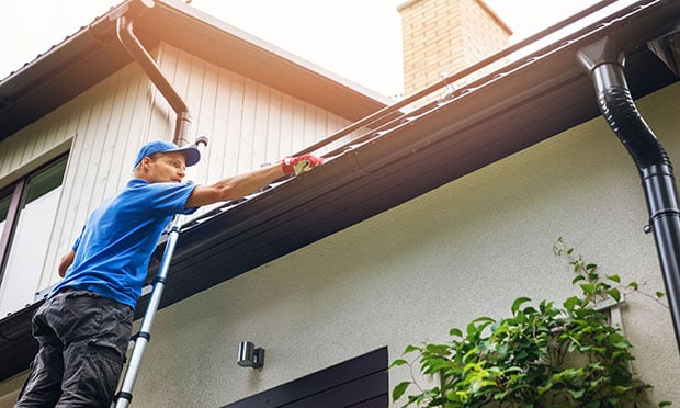 Man on ladder cleaning gutters