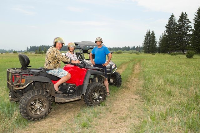 Three people with helmets in rural area riding ATVs 