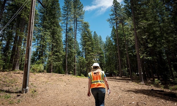 A Pacific Gas & Electric Co. (PG&E) employee walks past Pacific Gas & Electric Co. (PG&E) power lines in Nevada City, California, U.S., on Wednesday, June 12, 2019. (Photo: David Paul Morris/Bloomberg)