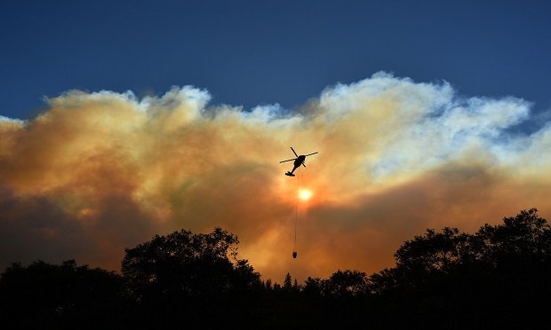TOPSHOT - A helicopter passes by the sun as it makes a water drop in the Feather River Canyon, east of Paradise, California on November 11, 2018. (Photo by Josh Edelson / AFP) (Photo credit should read JOSH EDELSON/AFP/Getty Images)