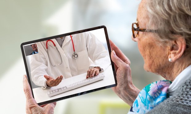 Senior woman consults a e-health doctor with tablet computer sitting in soft chair. In touchscreen, male doctor: With telehealth application patient can reach relevant specialist remotely. (Photo: by JPC-PROD/Shutterstock)