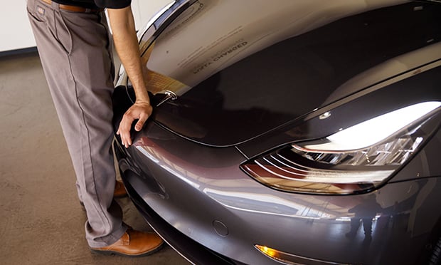 An employee closes the front hood of a Tesla Inc. Model 3 electric vehicle at the company's showroom in Newport Beach, California.