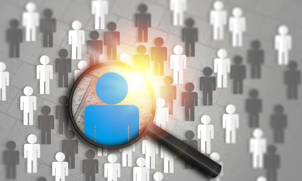 A bunch of gray and white cartoon people are spread across a gray background. A magnifying glass is held in front of them, magnifying one blue person. 