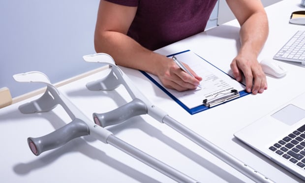 Disabled Male Patient Filling Insurance Claim Form Over Desk With Crutches