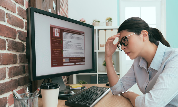 An office worker looks exasperated as an alert about ransomware takes up the screen of their computer.