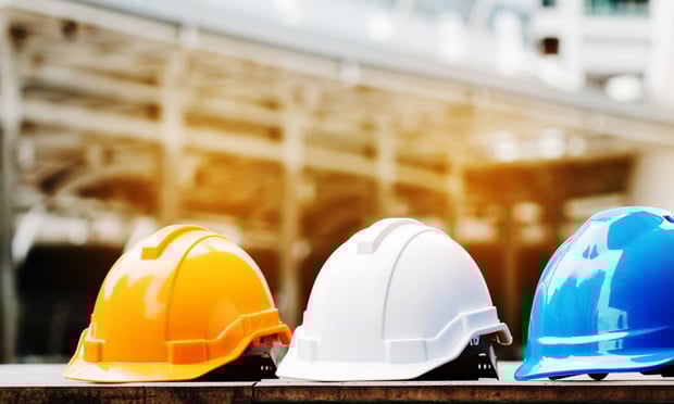 Three hard hats, one orange, one white, and one blue, sit side-by-side at a construction site.