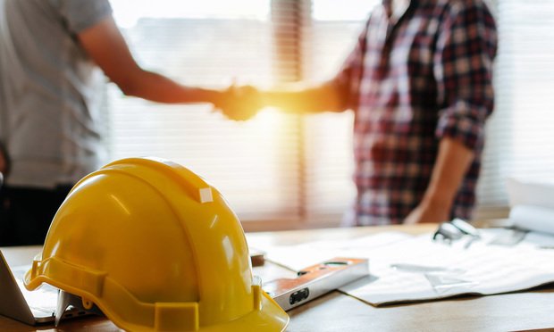 Two people shaking hands on a job site, a hard hat and tools are in the foreground.