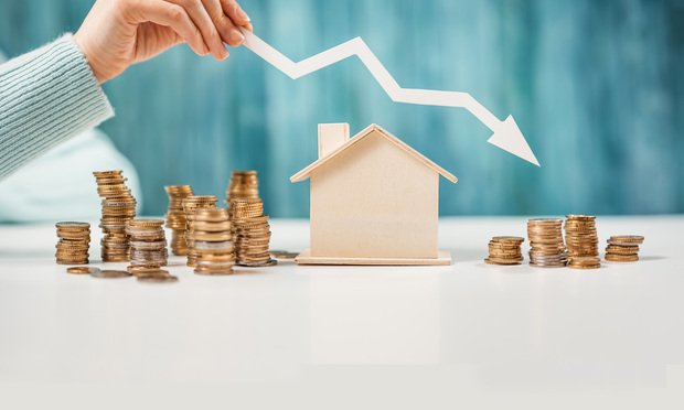 Change stacked next to a toy wooden house, a downward point air is above the home.