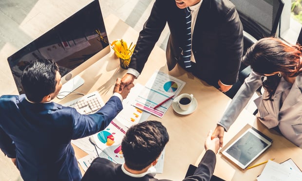 A group of four business people shake hands across a table.