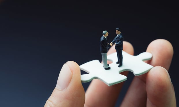Business success strategy with collaboration, teamwork or negotiation jigsaw key, miniature people businessmen handshaking on white jigsaw puzzle piece in real human hand, dark black background. Credit: Nuthawut/Adobe Stock