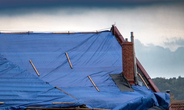 The protective tarpaulin on the roof flutters at the storm with rain.