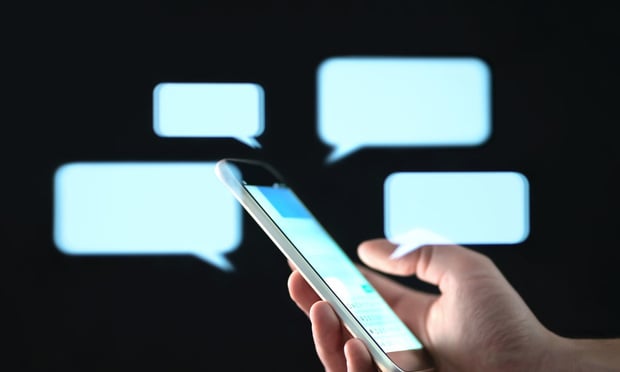 A hand holds a phone with illustrations of text bubbles in the background.