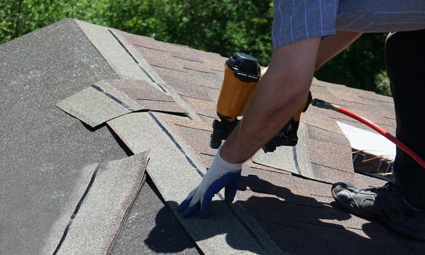 Roofer nailing asphalt shingles with air gun.