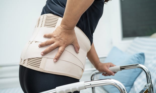 A person wearing a back brace and using a walker, as if their spine is injured.
