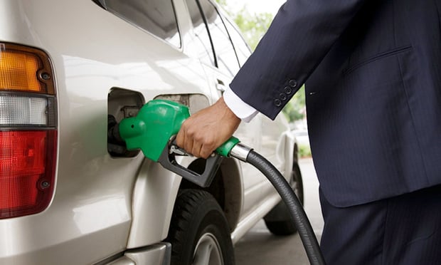 A person in a suit pumps gas into their vehicle.