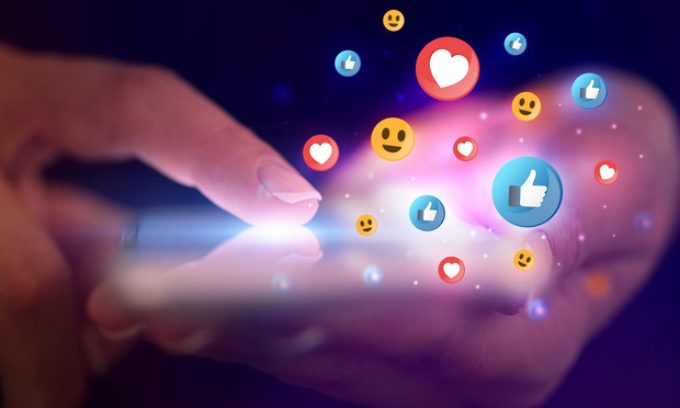 A close-up of a hand holding a smart phone with emoji graphics floating around in the foreground.