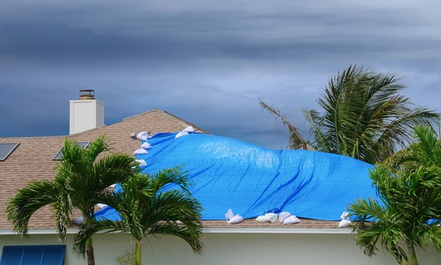 Storm damaged roof on house with a blue plastic tarp over hole in the shingles and rooftop. Credit: Michael O'Keene/Adobe Stock