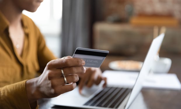 A person holds up a credit or debit card as they sit in front of their laptop.