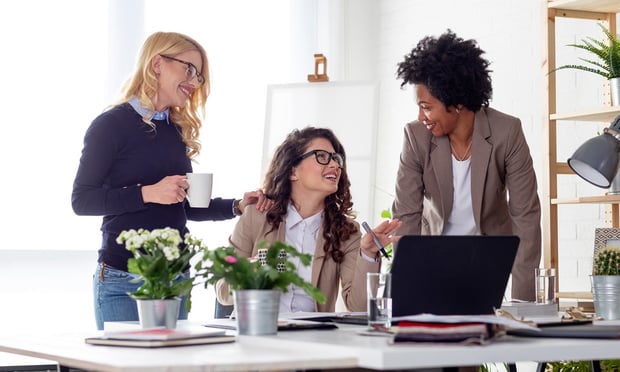 Three women speak to each other in an office as they work.