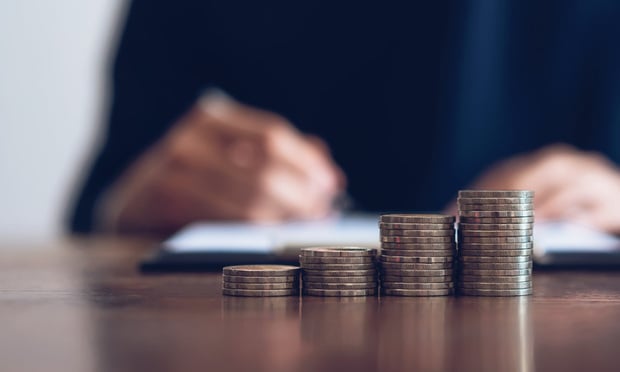 Four piles of coins are arranged on a desk in front of a person's hands. The stacks of coins get taller from left to right.