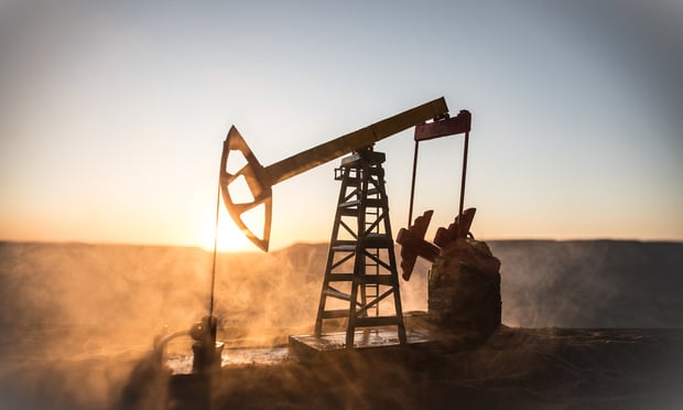 An oil rig is silhouetted by the sunset.
