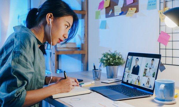 A person takes notes while on a video call as they work at home.