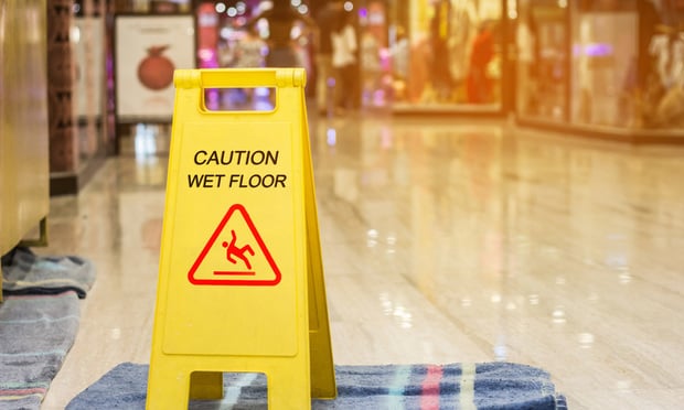 A wet floor sign sits on top of a towel on the floor of a mall.