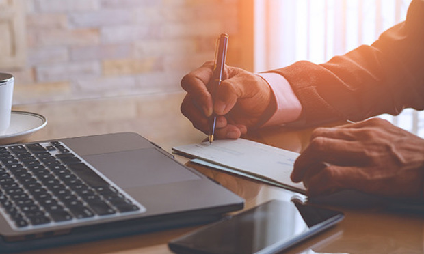 A person writes a check on a desk next to a laptop.
