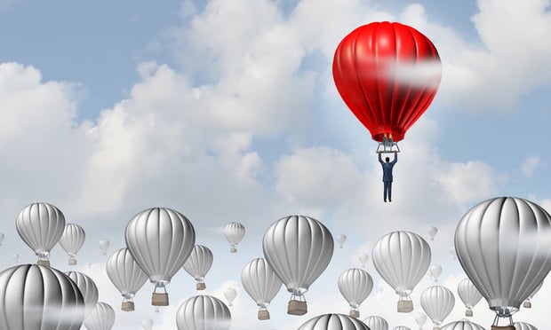A red hot air balloon with a man dangling from it soars above a group of silver hot air balloons in the sky.