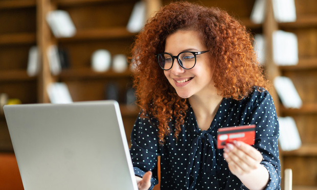 A person holds a credit card in their hand as they type on their laptop.