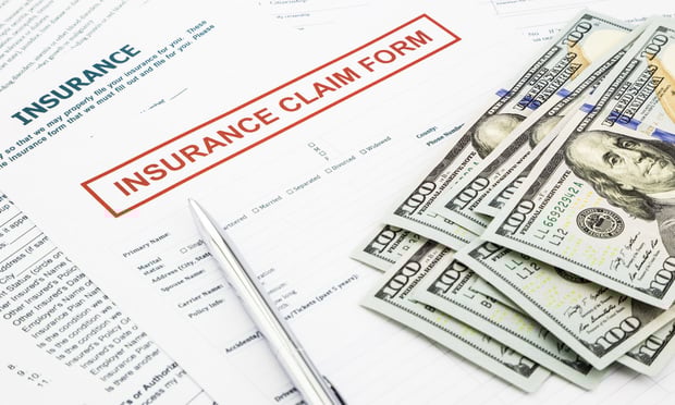 A pile of $100 bills on top of an insurance claim form.