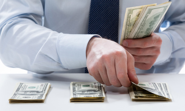 A person counts out stacks of $100 bills on a desk.