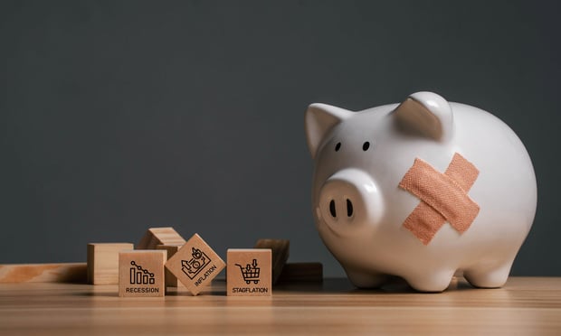 A piggy bank with a bandage on its side next to a pile of fallen blocks with recession-related words on them.