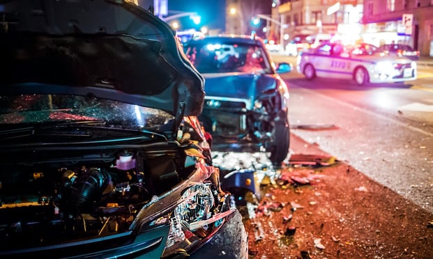 Two crashed cars in a road with a police car behind them.