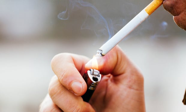 A close-up of a person lighting a cigarette with a lighter.