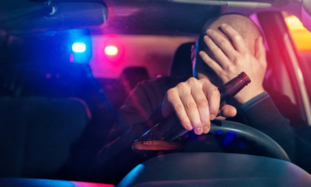 Upset male driver is caught driving under alcohol influence. Man covering his face from police car light.