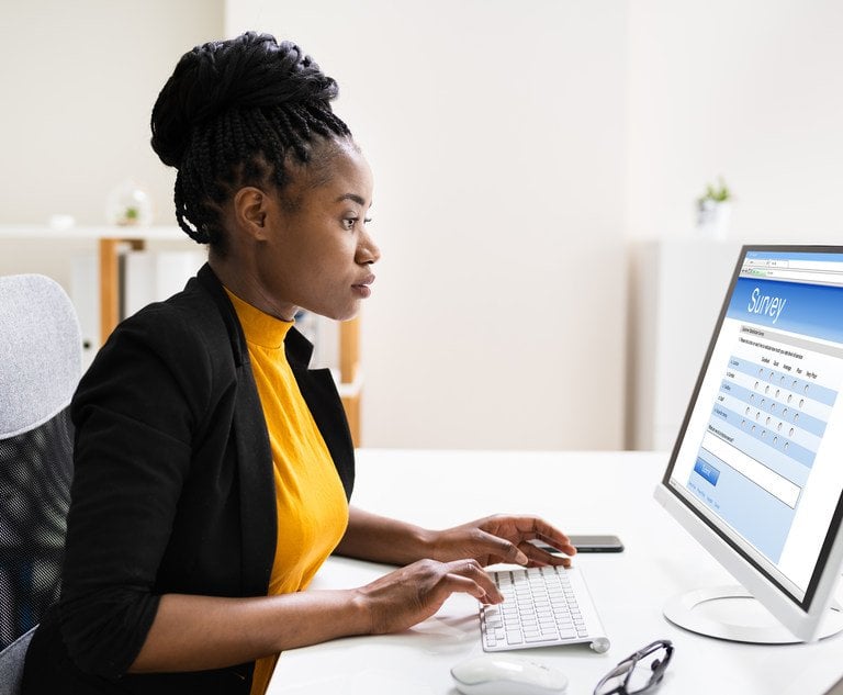 A woman sits in front of a desktop computer, taking an online survey.