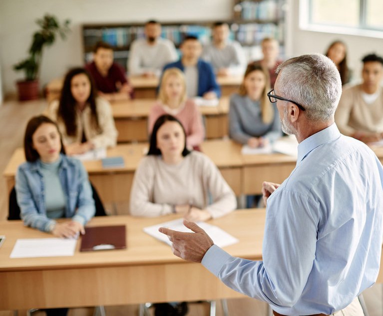 A group of students listen to their professor lecture in a classroom.