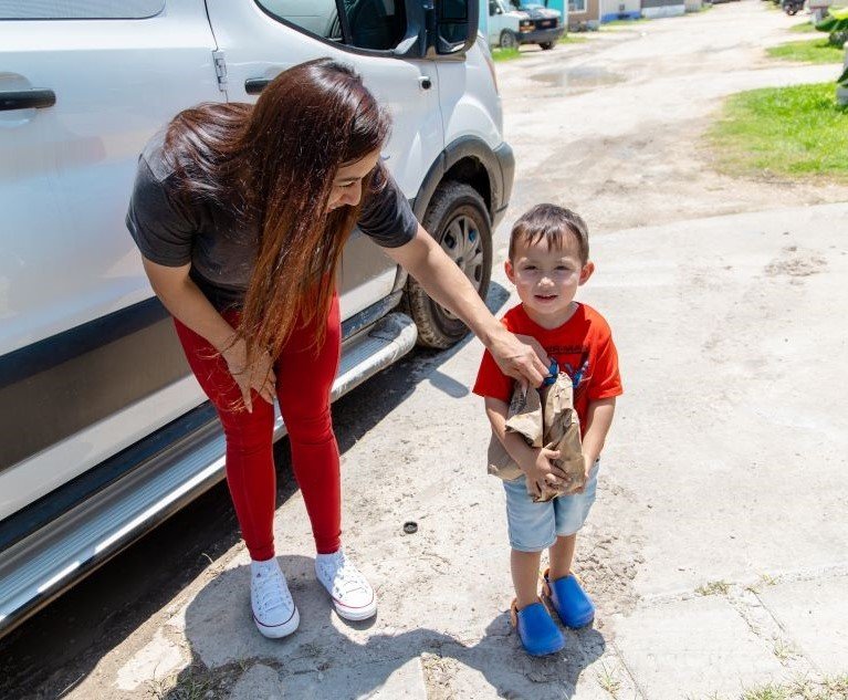A child is handed a bag of food by an adult .